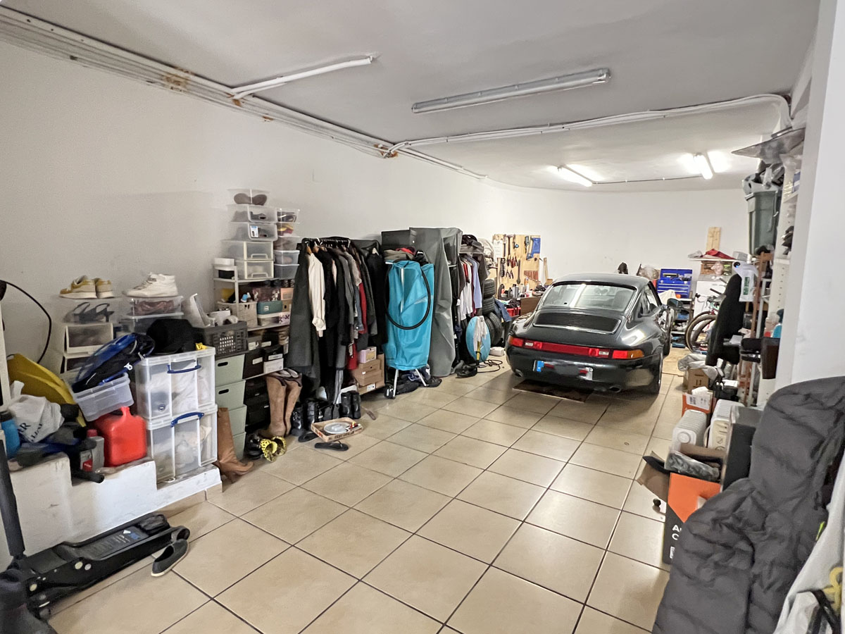 Garage spacieux avec sol carrelé, éclairage fluorescent et de nombreux rangements organisés pour véhicules et équipements divers.