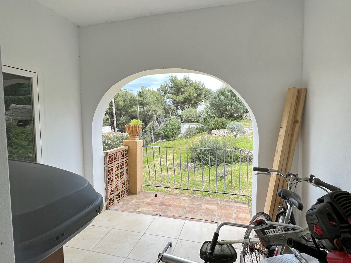 Porche couvert doté d'une arche méditerranéenne typique ouvrant sur le jardin. Espace fonctionnel avec carrelage clair et garde-corps en métal.