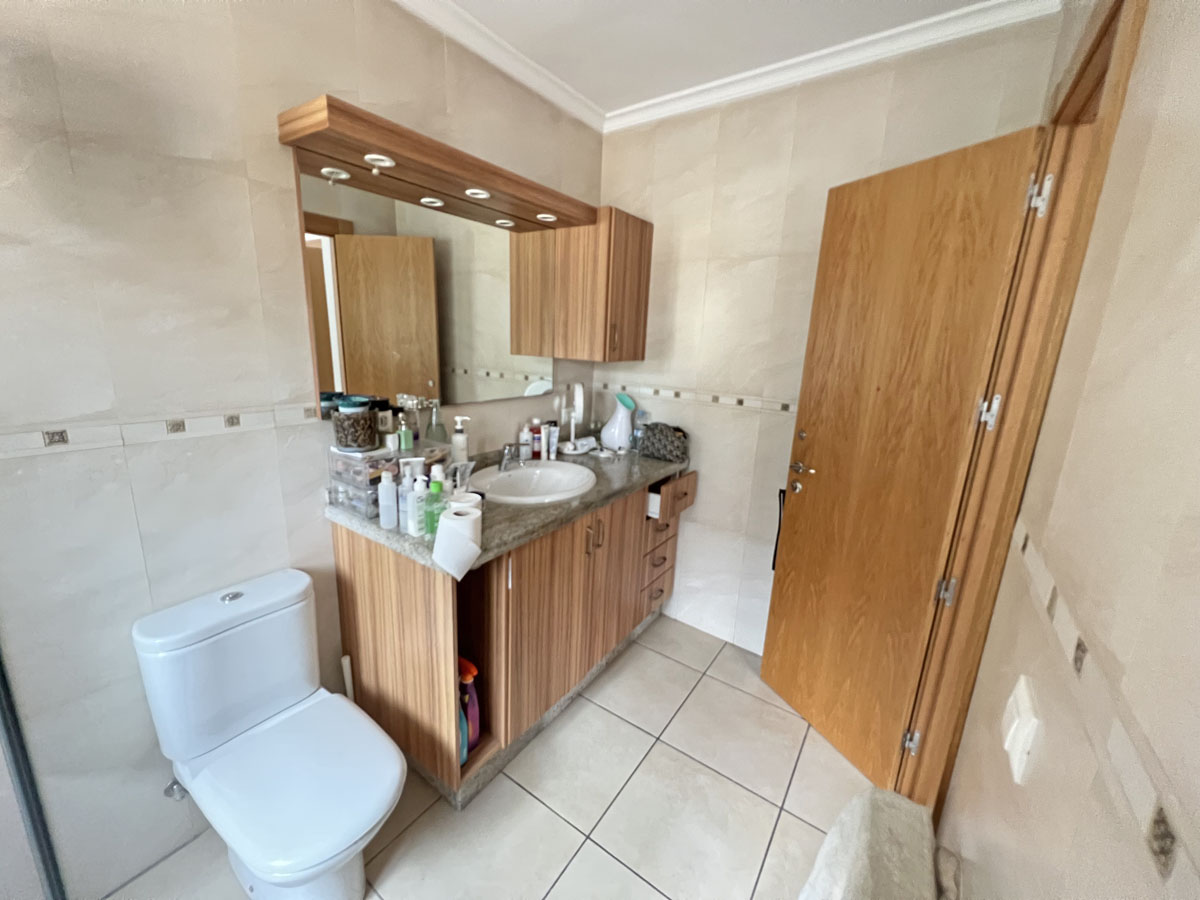 Salle de bain avec meuble vasque en bois, plan de travail en granit et miroir avec éclairage intégré. Murs carrelés dans des tons crème avec frise décorative.