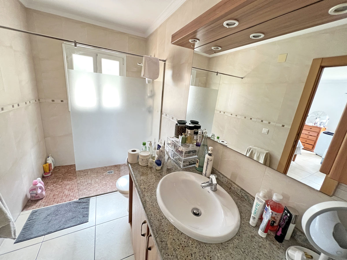 Salle de bain équipée d'un plan de travail en granit, d'un meuble en bois et d'une douche à l'italienne avec paroi dépolie et sol en mosaïque rouge.