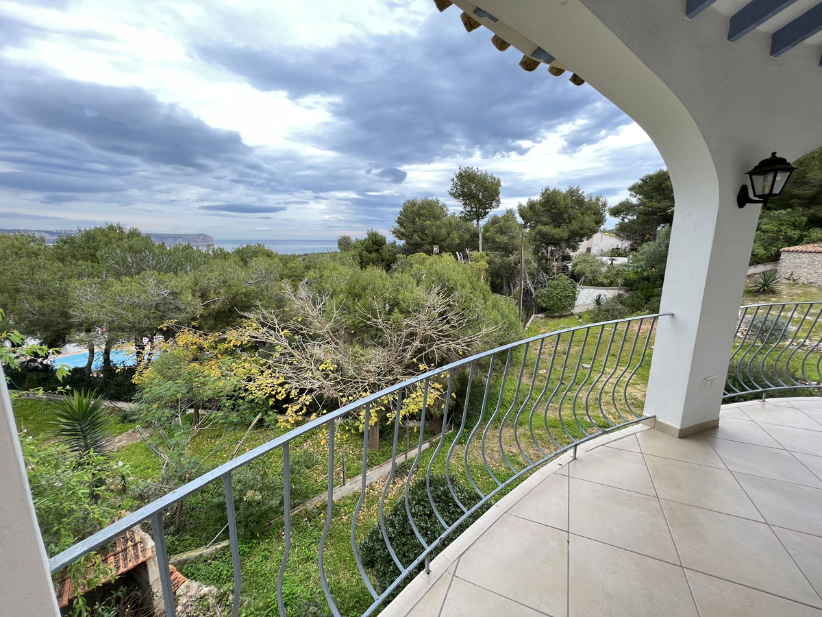 Terrasse couverte avec carrelage clair et garde-corps en fer, offrant une vue dégagée sur la mer Méditerranée et le Cap San Antonio à Jávea.