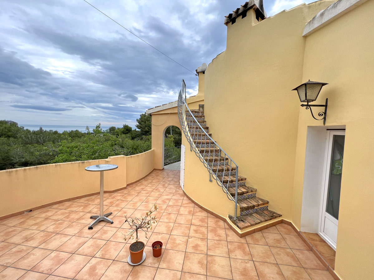 Terrasse extérieure avec sol en terre cuite et escalier courbe orné de carreaux décoratifs. Elle offre une vue dégagée sur la mer Méditerranée et la pinède environnante.