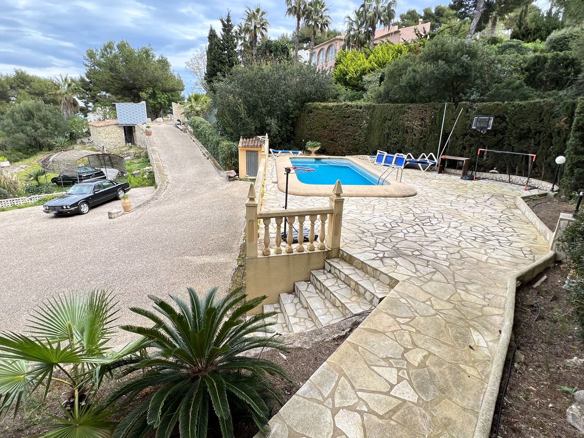 Terrasse surélevée en pierre naturelle avec piscine, bordée d'une balustrade et d'une allée menant à un espace de stationnement privé.