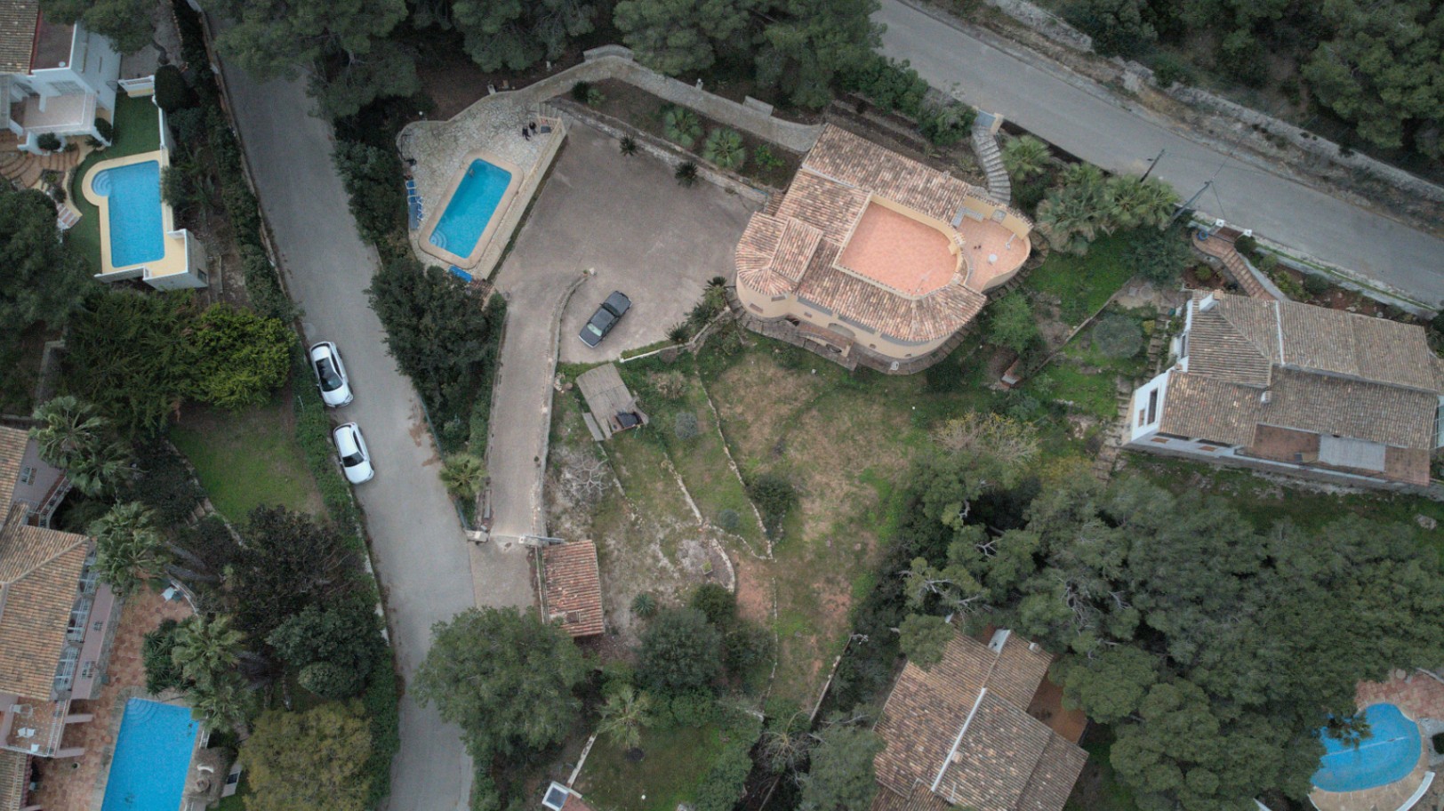 Vue aérienne par drone révélant l'agencement de la parcelle, la piscine rectangulaire, la grande zone de stationnement et le jardin méditerranéen en terrasses.