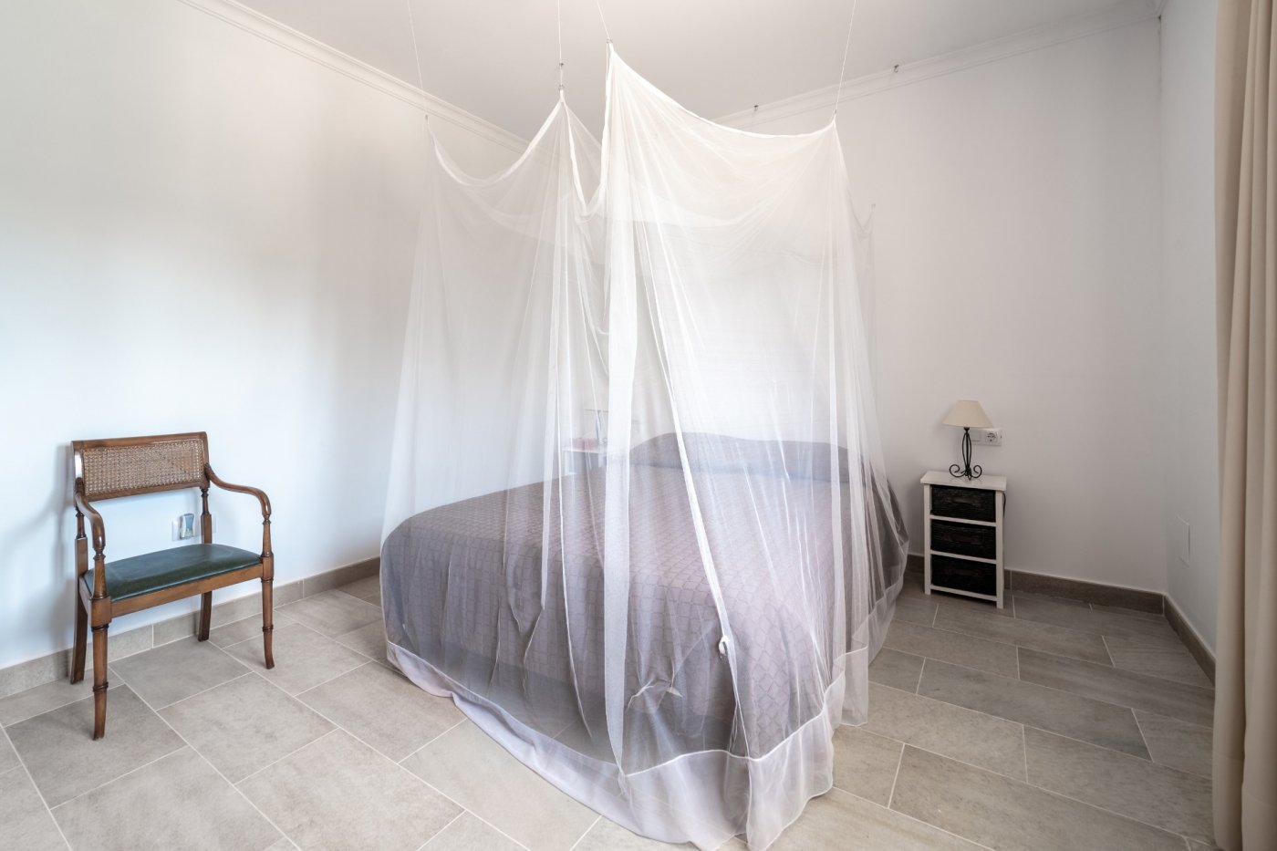 Chambre avec lit double protégé par une moustiquaire, sol en grès cérame et mobilier d'appoint de style classique.