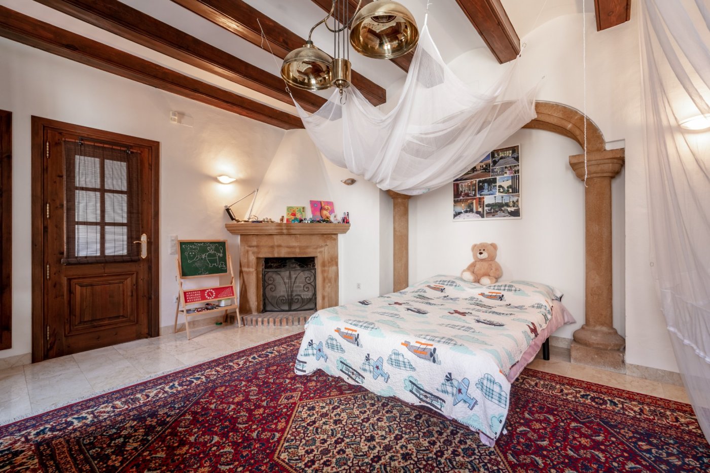 Chambre avec poutres apparentes, cheminée en pierre traditionnelle et une arche en pierre de Tosca encadrant l'espace nuit.