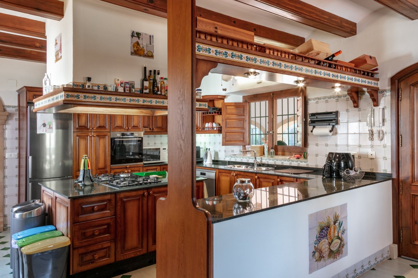 Cuisine rustique avec poutres apparentes, plans de travail en granit sombre et azulejos traditionnels. Elle comprend un îlot central et des finitions en bois massif.