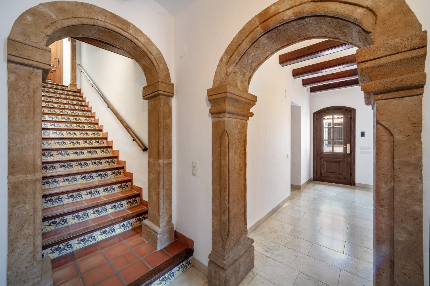 Hall d'entrée avec arches en pierre de Tosca, escalier orné de carreaux traditionnels et plafonds avec poutres en bois apparentes.