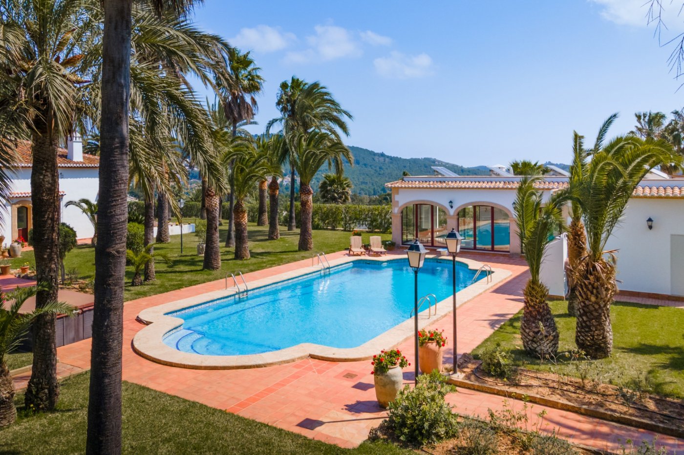Piscine de 16x7m avec terrasse en terre cuite, entourée de palmiers et d'une maison d'invités aux arches traditionnelles et panneaux solaires.