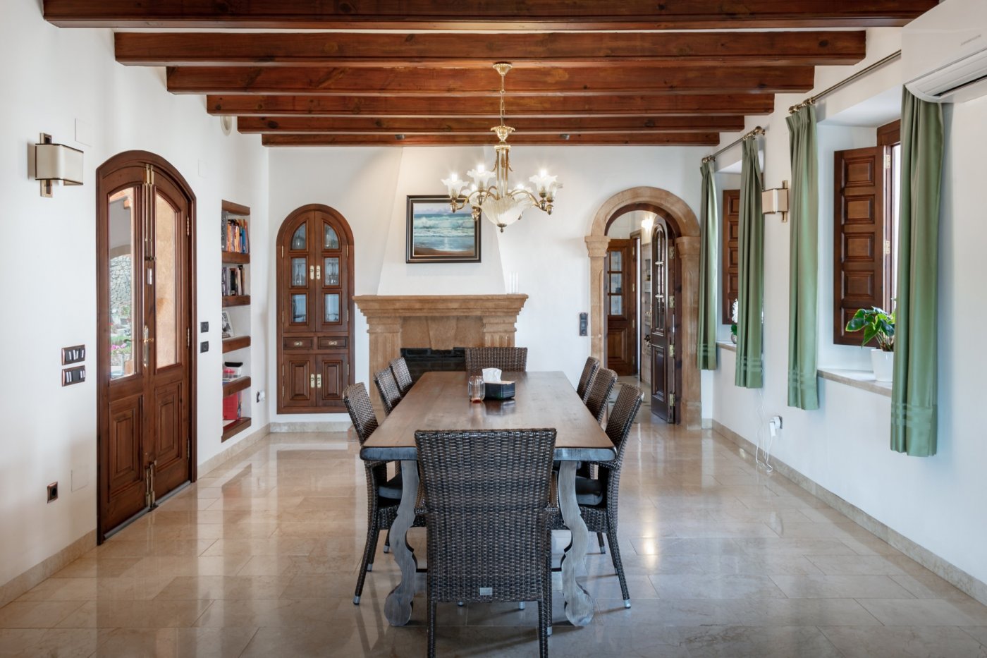Salle à manger avec poutres apparentes, cheminée en pierre de Tosca et sol en marbre. La pièce se distingue par ses arches en pierre et son mobilier en bois.