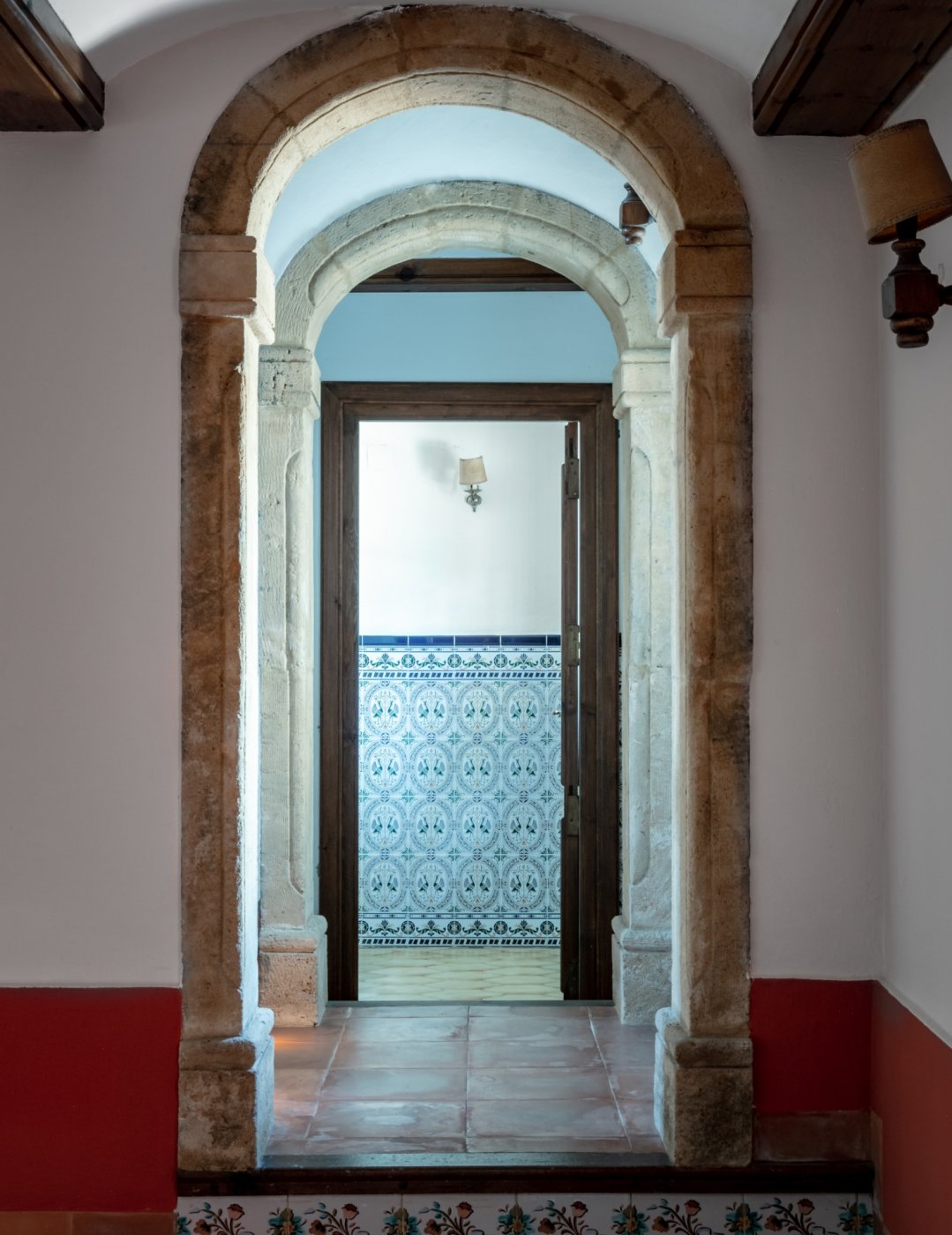 Vue à travers des arches en pierre de Tosca naturelle menant à une pièce avec des carreaux muraux décoratifs traditionnels et un sol en terre cuite.