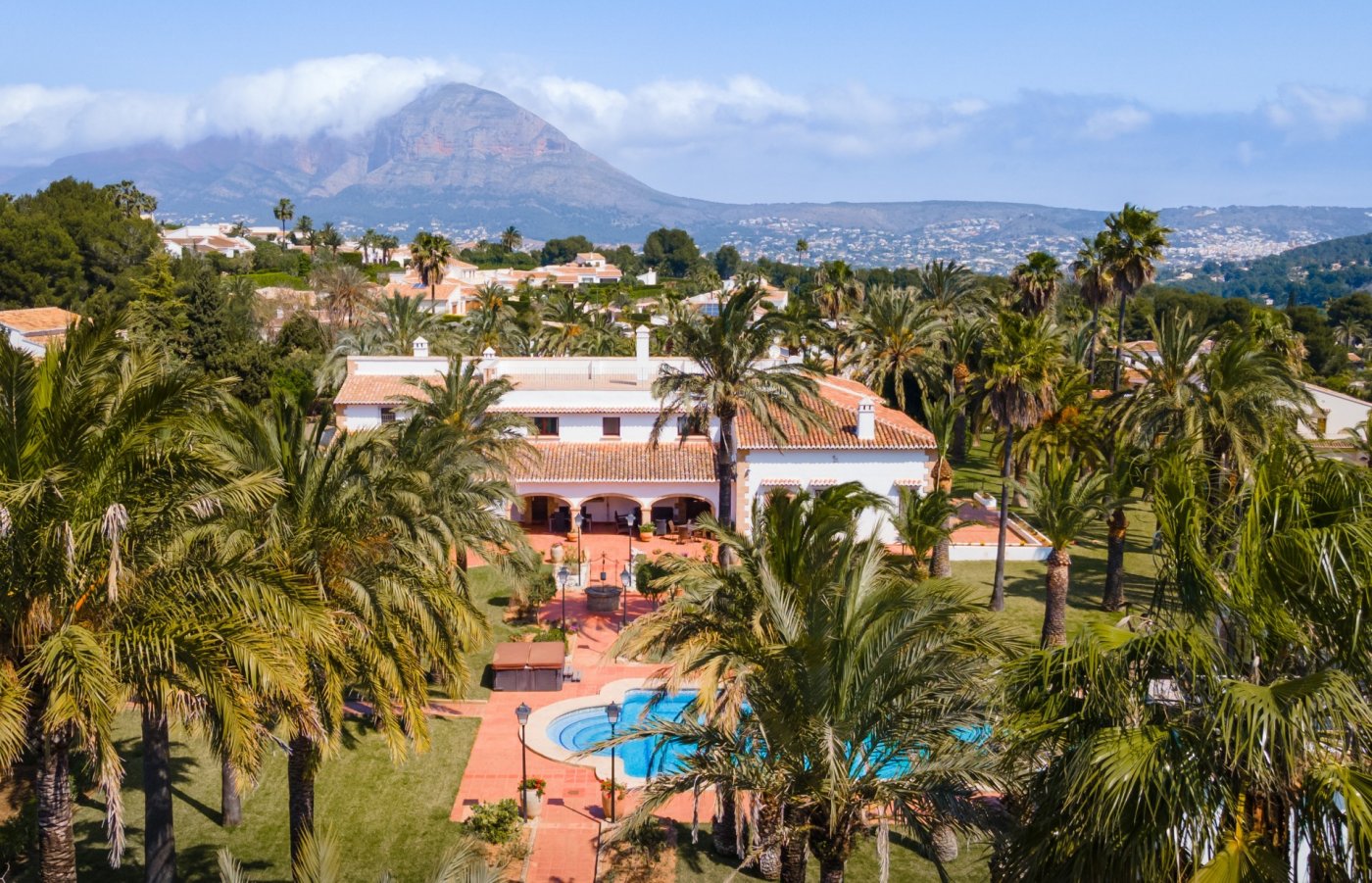 Vue aérienne de la villa méditerranéenne avec sa grande piscine, son jardin de palmiers et une vue dégagée sur le mont Montgó en arrière-plan.