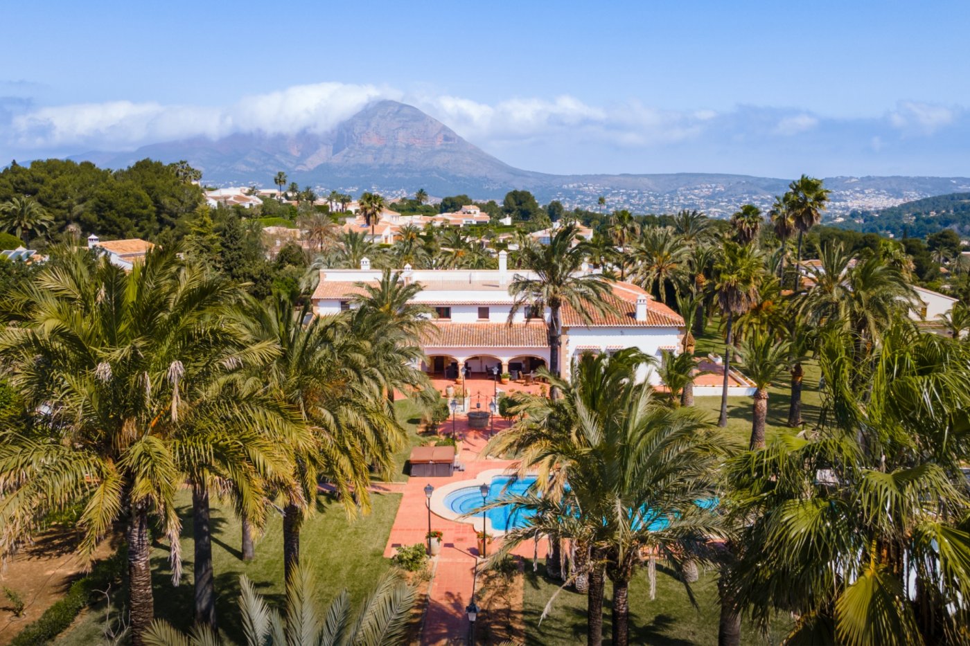 Vue aérienne de la villa méditerranéenne avec son vaste jardin de palmiers, sa piscine privée et une vue panoramique sur le mont Montgó.