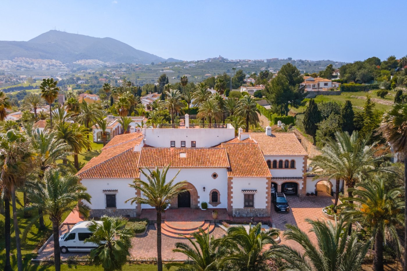 Vue aérienne de la villa méditerranéenne avec toits en tuiles, arches en pierre de Tosca et un vaste terrain arboré de palmiers offrant une vue sur la vallée.