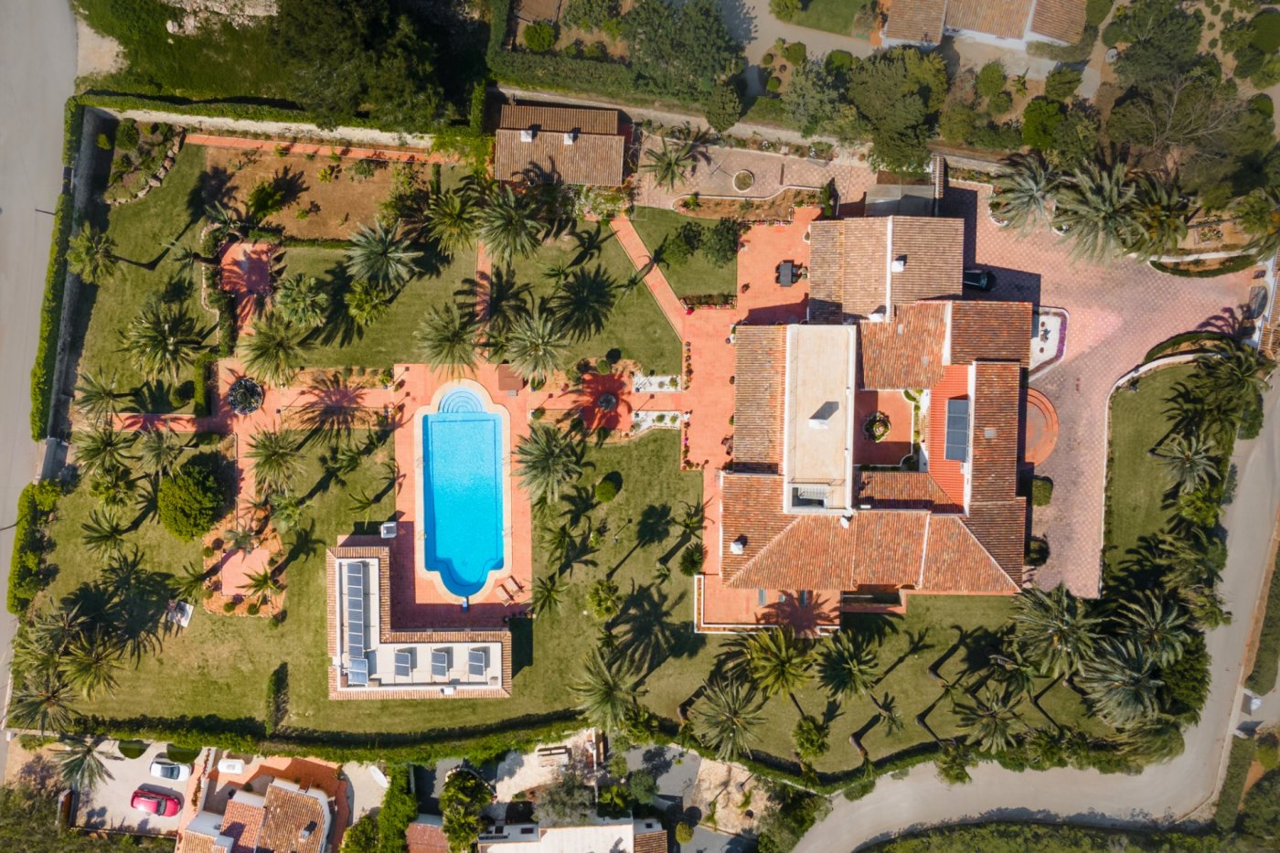 Vue aérienne du domaine révélant la villa principale avec patio central, la piscine et le vaste jardin paysager parsemé de nombreux palmiers.