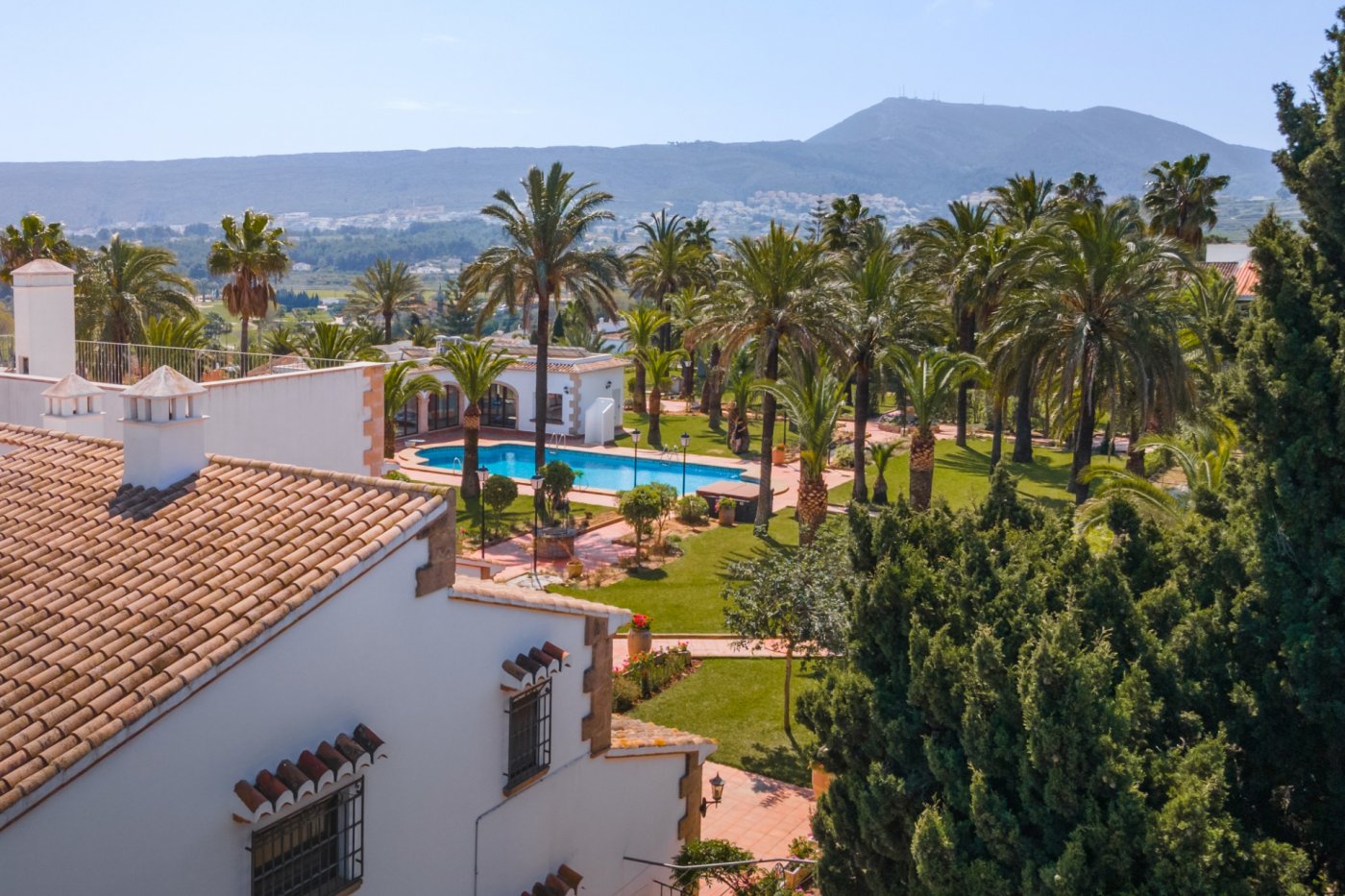 Vue en hauteur sur le domaine méditerranéen, incluant la piscine de 16x7m, la maison d'amis et un jardin luxuriant de palmiers avec vue sur la vallée.