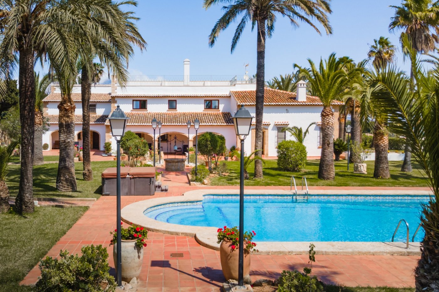 Vue extérieure de la piscine de 16x7m et du jardin paysager avec palmiers, mettant en valeur la villa méditerranéenne aux arches en pierre de Tosca.