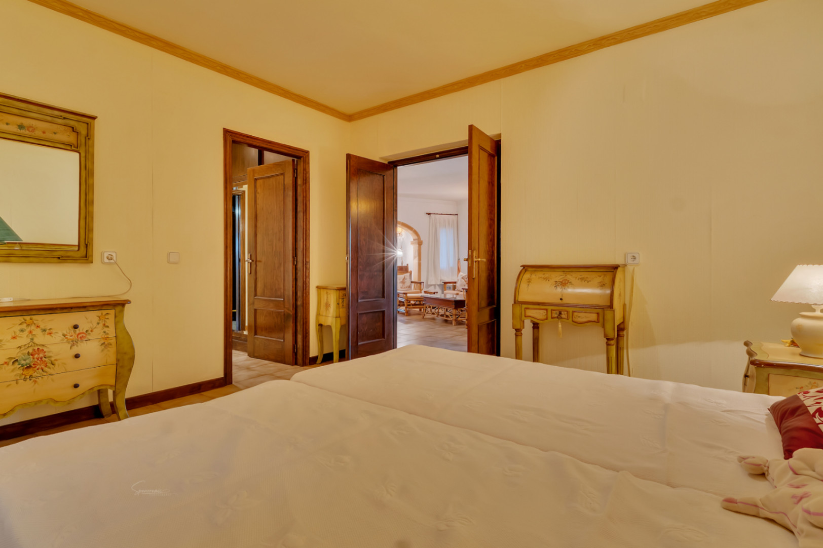 Chambre avec mobilier peint de style classique, portes en bois massif et vue sur le salon principal à travers une arche en pierre naturelle.