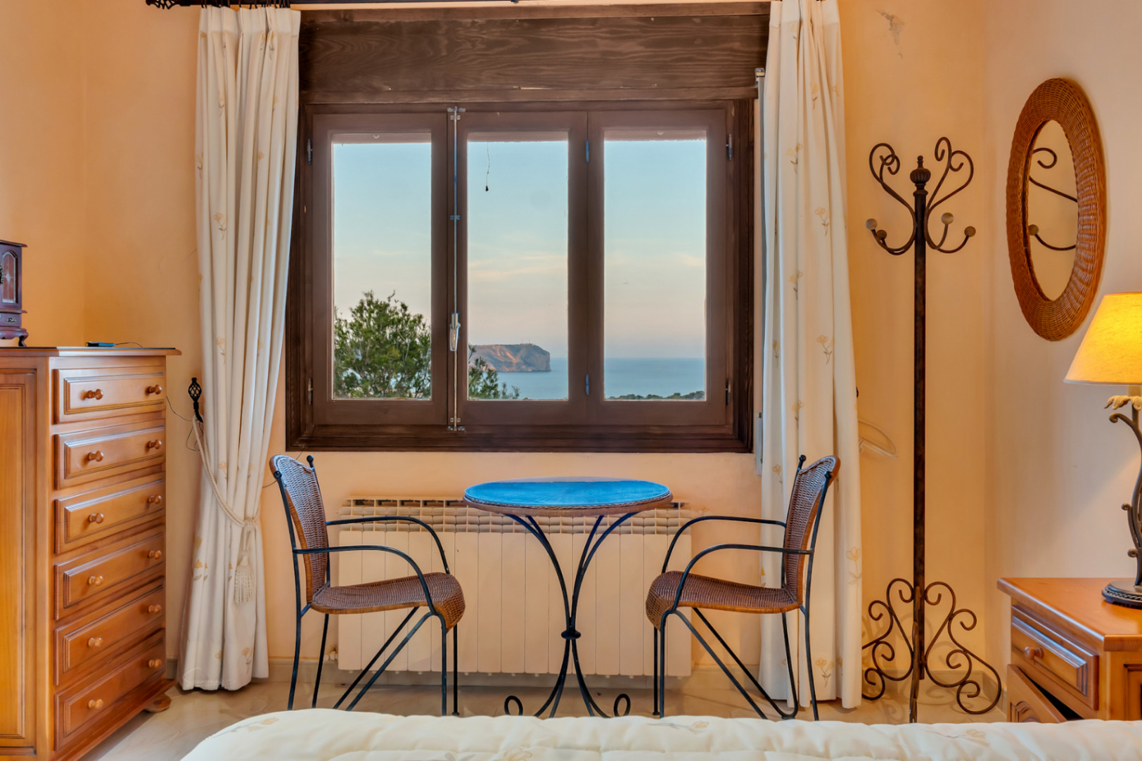 Coin salon de chambre avec fenêtre offrant une vue sur le Cabo San Antonio. Comprend une commode en bois, un radiateur et un miroir en osier.
