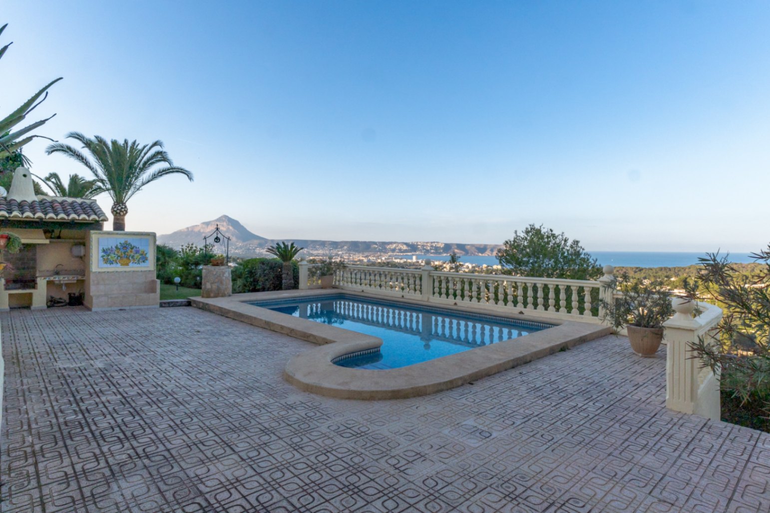 Espace piscine avec escalier romain et terrasse carrelée, bordé d'une balustrade classique offrant une vue panoramique sur la baie de Jávea et le Montgó.