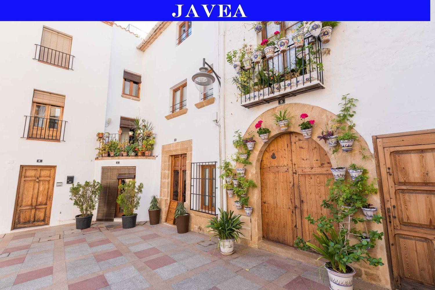 Façade traditionnelle dans la vieille ville de Jávea avec portes en bois, arches en pierre de tosca et pots de fleurs décoratifs sur murs blancs.
