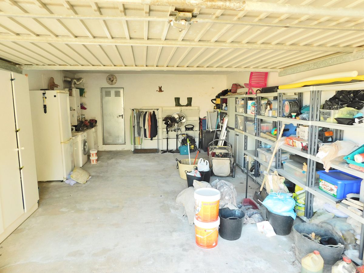 Grand garage avec sol en béton, étagères de rangement métalliques et un espace buanderie équipé d'un lave-linge et d'un réfrigérateur.