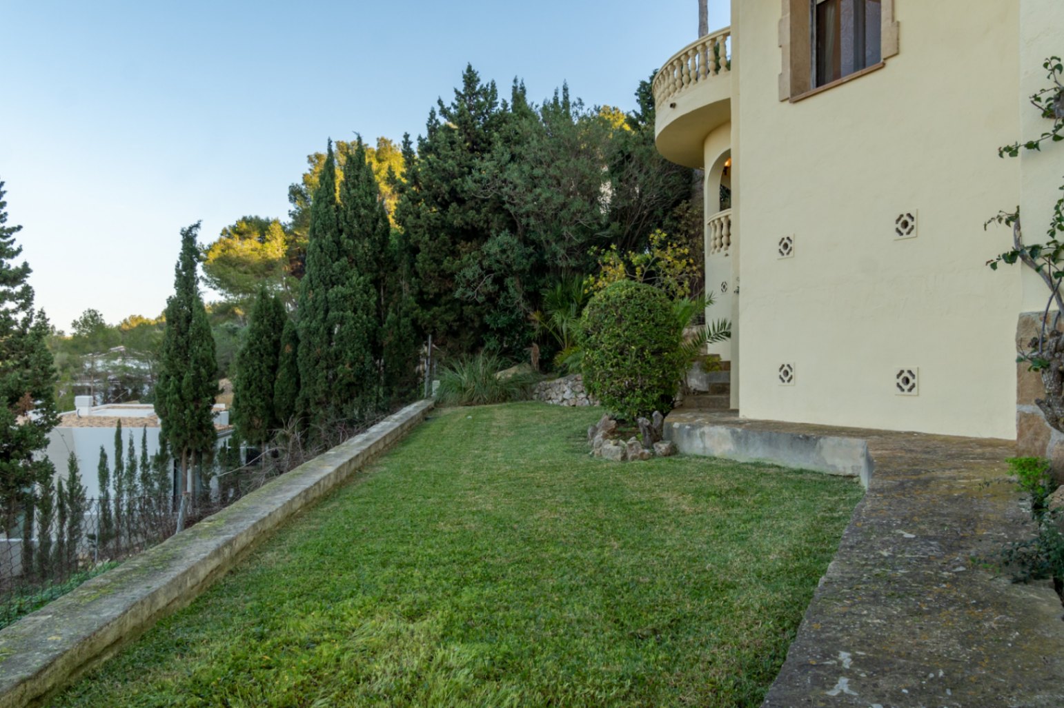 Jardin latéral avec pelouse entretenue, bordé de cyprès et de végétation méditerranéenne près de la façade de la villa.