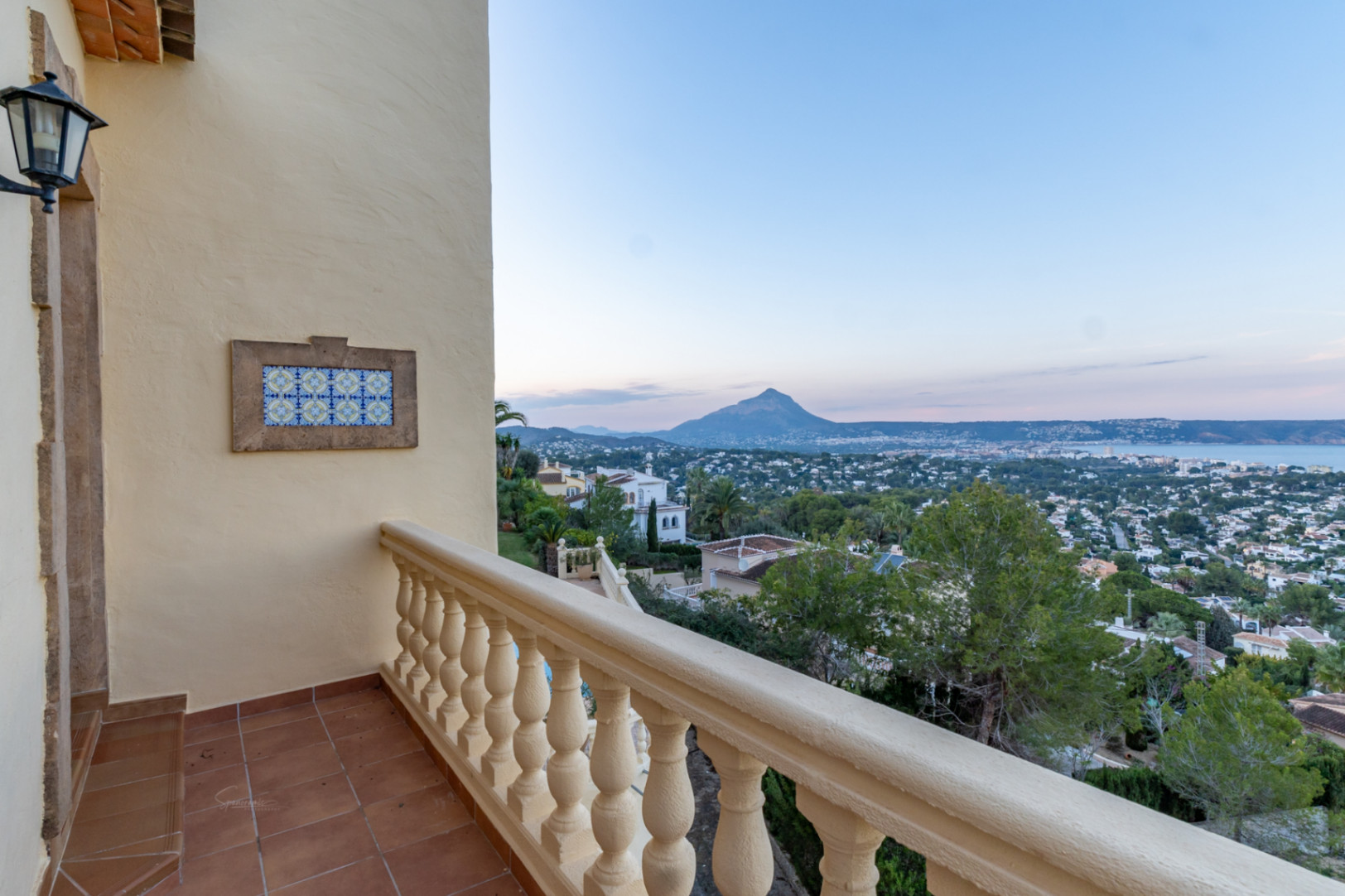 Terrasse avec carrelage en terre cuite et balustrade classique, offrant une vue panoramique sur le Montgó et la baie de Jávea. Détail mural en azulejos décoratifs.