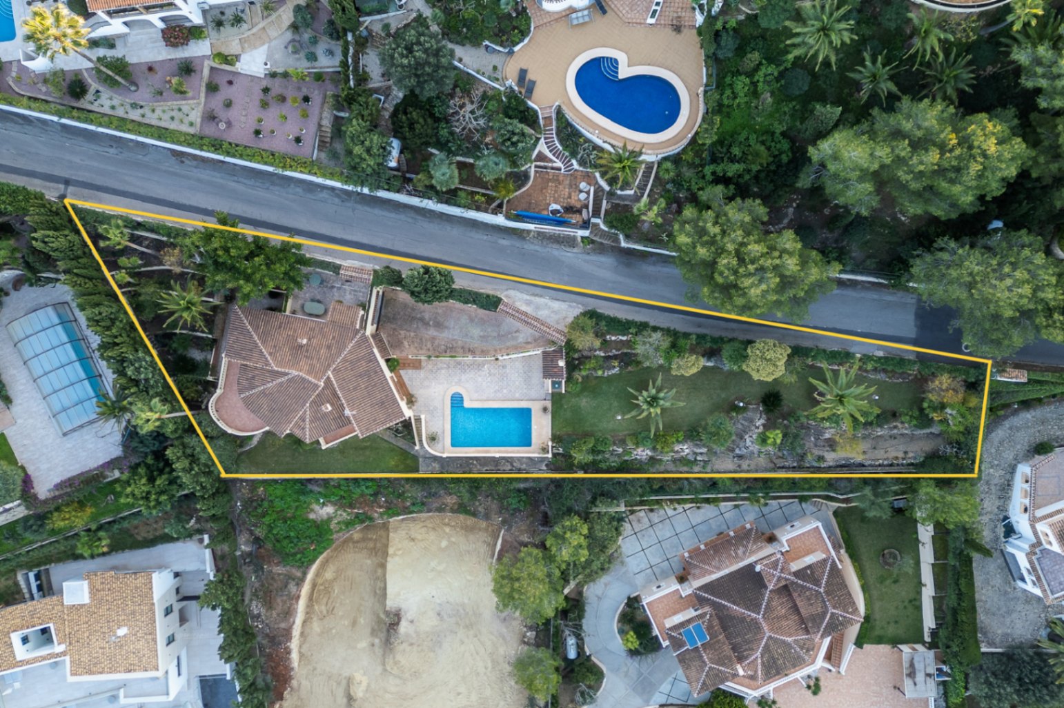 Vue aérienne délimitée de la propriété, illustrant la piscine en L, le jardin méditerranéen avec palmiers et l'agencement des toitures en tuiles de la villa.