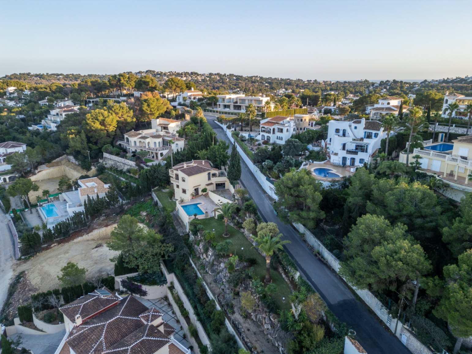 Vue aérienne du quartier résidentiel Costa Nova Panorama à Jávea, présentant des villas méditerranéennes avec piscines privées au cœur d'une pinède verdoyante.