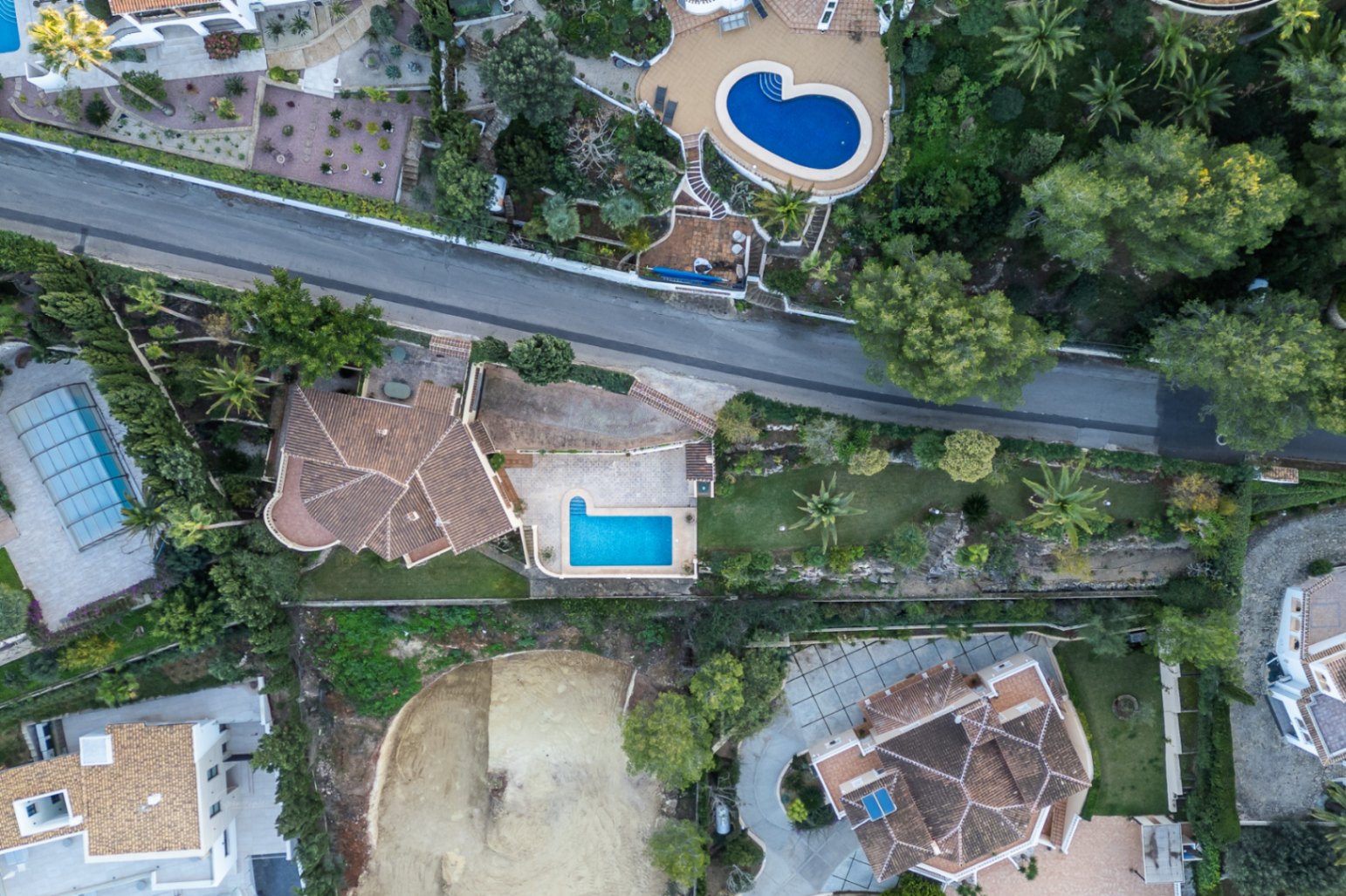 Vue aérienne zénithale de la villa montrant la disposition du terrain, la piscine rectangulaire, les terrasses pavées et le jardin méditerranéen avec palmiers.