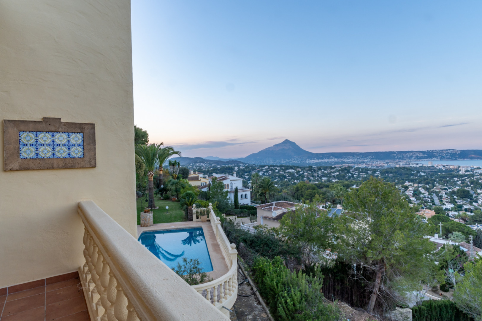 Vue panoramique depuis la terrasse supérieure sur la piscine, le jardin méditerranéen et la baie de Jávea, avec le mont Montgó se dessinant à l'horizon.