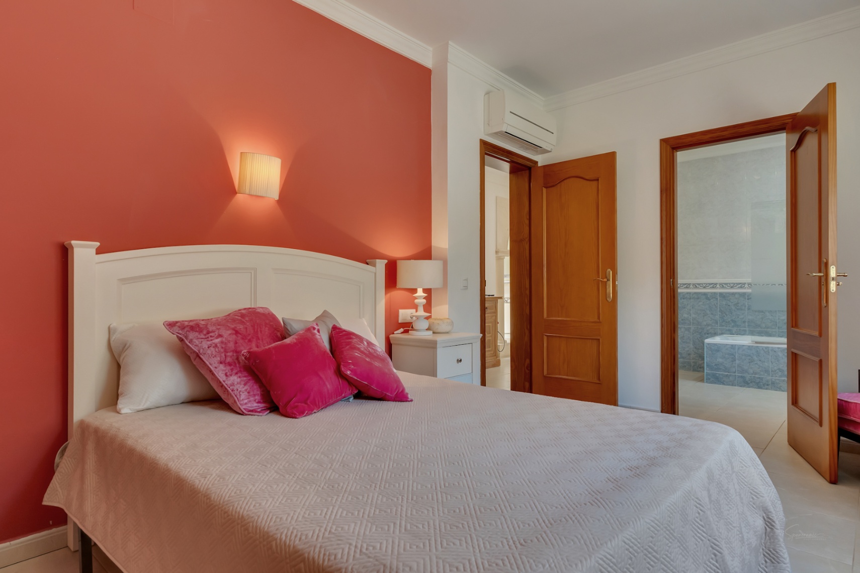 Chambre avec mur d'accent terre cuite, climatisation individuelle et salle de bains attenante équipée d'une baignoire et de carrelage bleu.