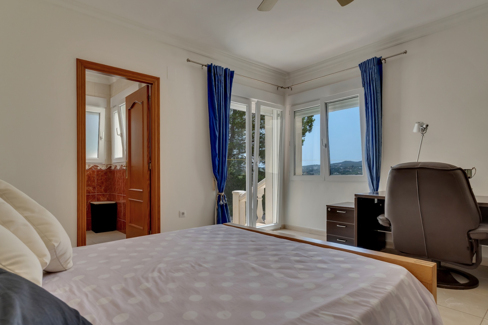 Chambre lumineuse avec coin bureau, accès à la terrasse et salle de bains attenante. Les grandes fenêtres offrent une vue dégagée sur les collines environnantes.