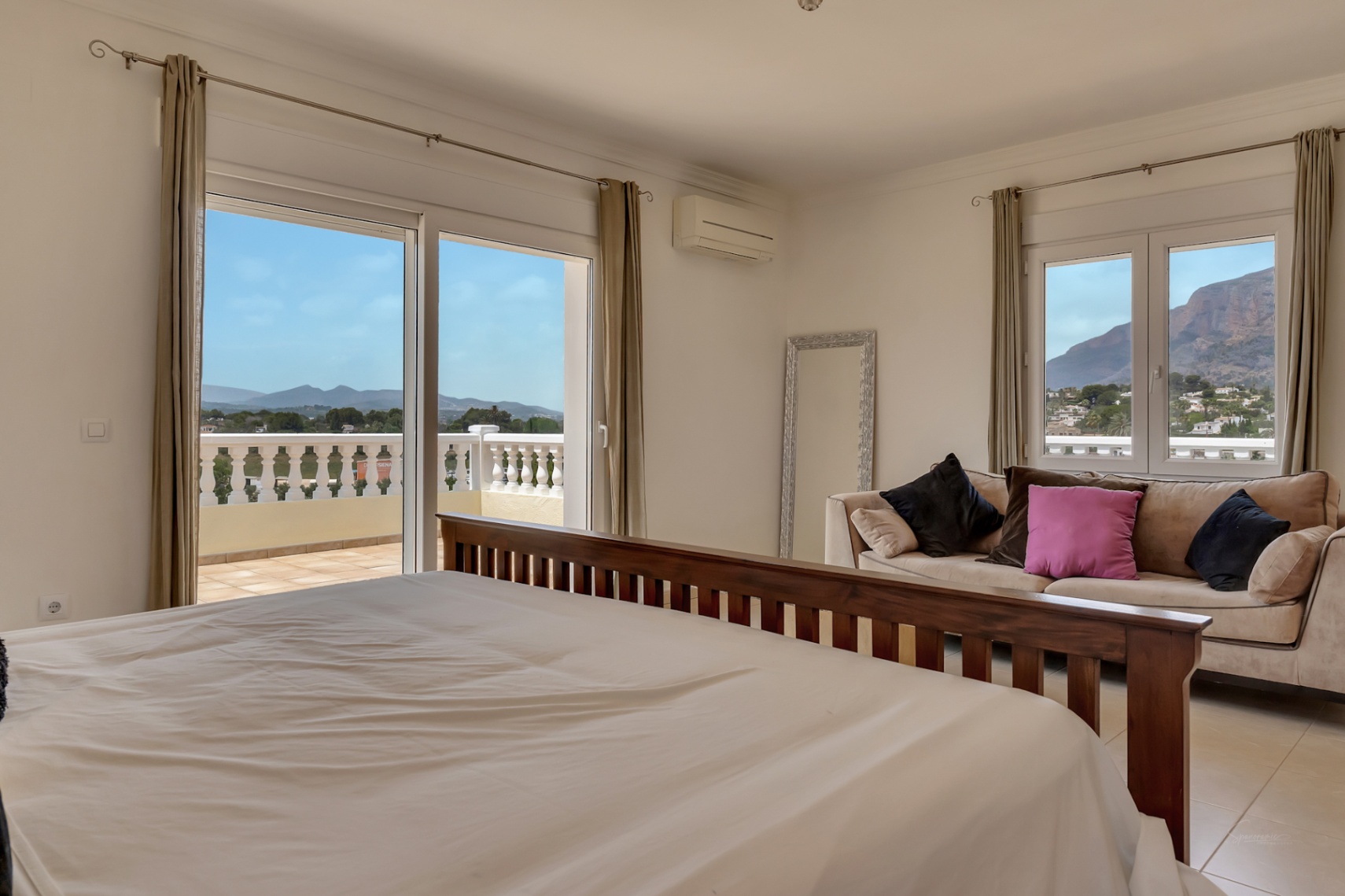 Chambre principale avec cadre de lit en bois, coin salon et accès terrasse offrant des vues panoramiques sur le Montgó et la vallée environnante.