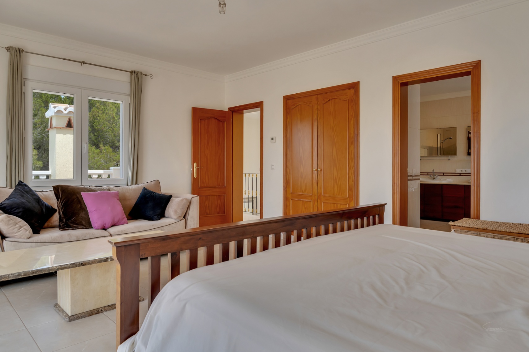 Chambre principale avec coin salon, placards intégrés en bois et salle de bains attenante. Elle dispose de carrelage au sol et d'une vue sur la nature environnante.