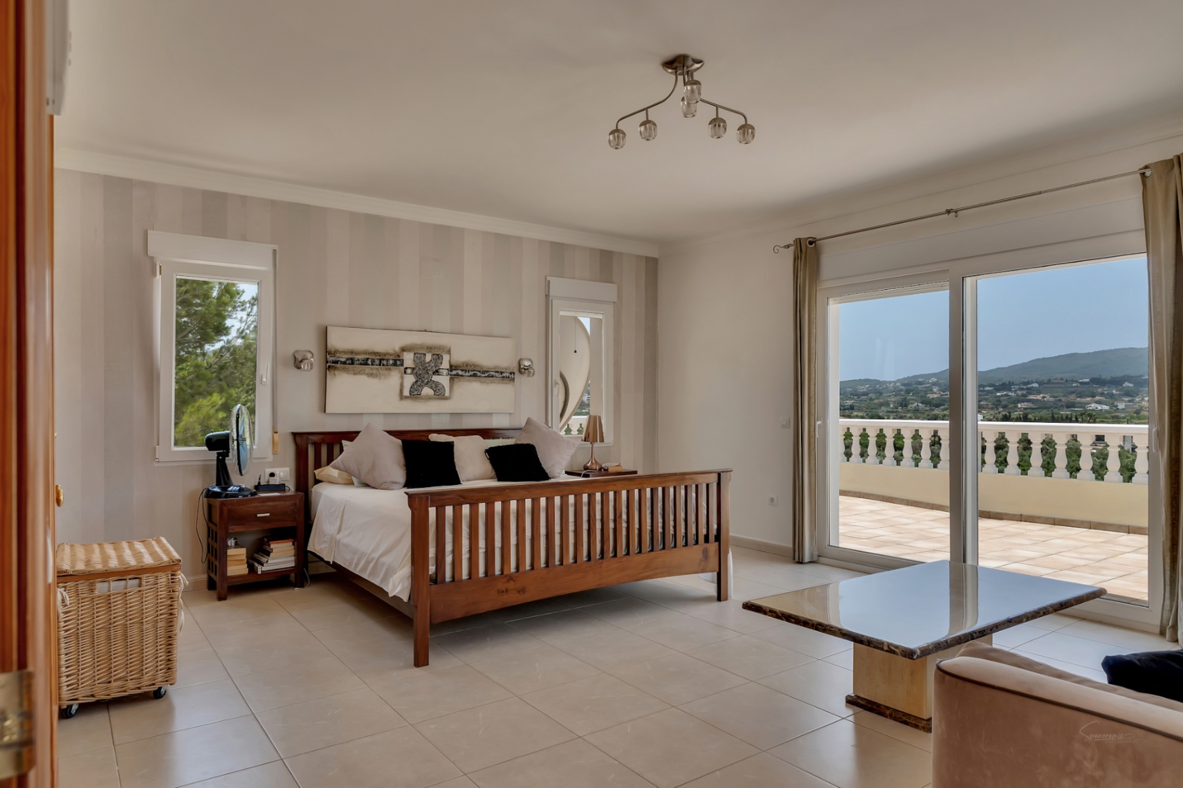 Chambre principale avec lit en bois, papier peint rayé et grandes baies vitrées ouvrant sur une terrasse privée offrant une vue panoramique sur la vallée.