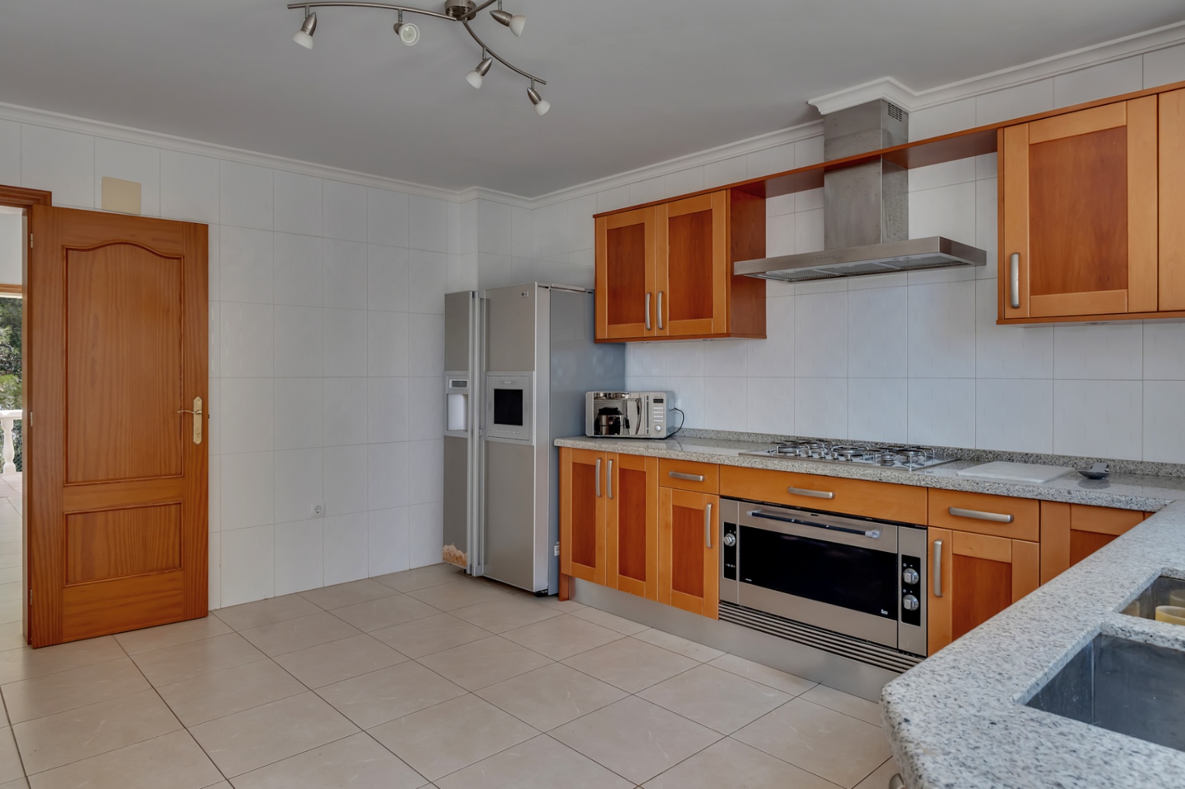 Cuisine équipée avec des meubles en bois, des plans de travail en granit gris et des appareils en acier inoxydable, dont un réfrigérateur américain et un large four.