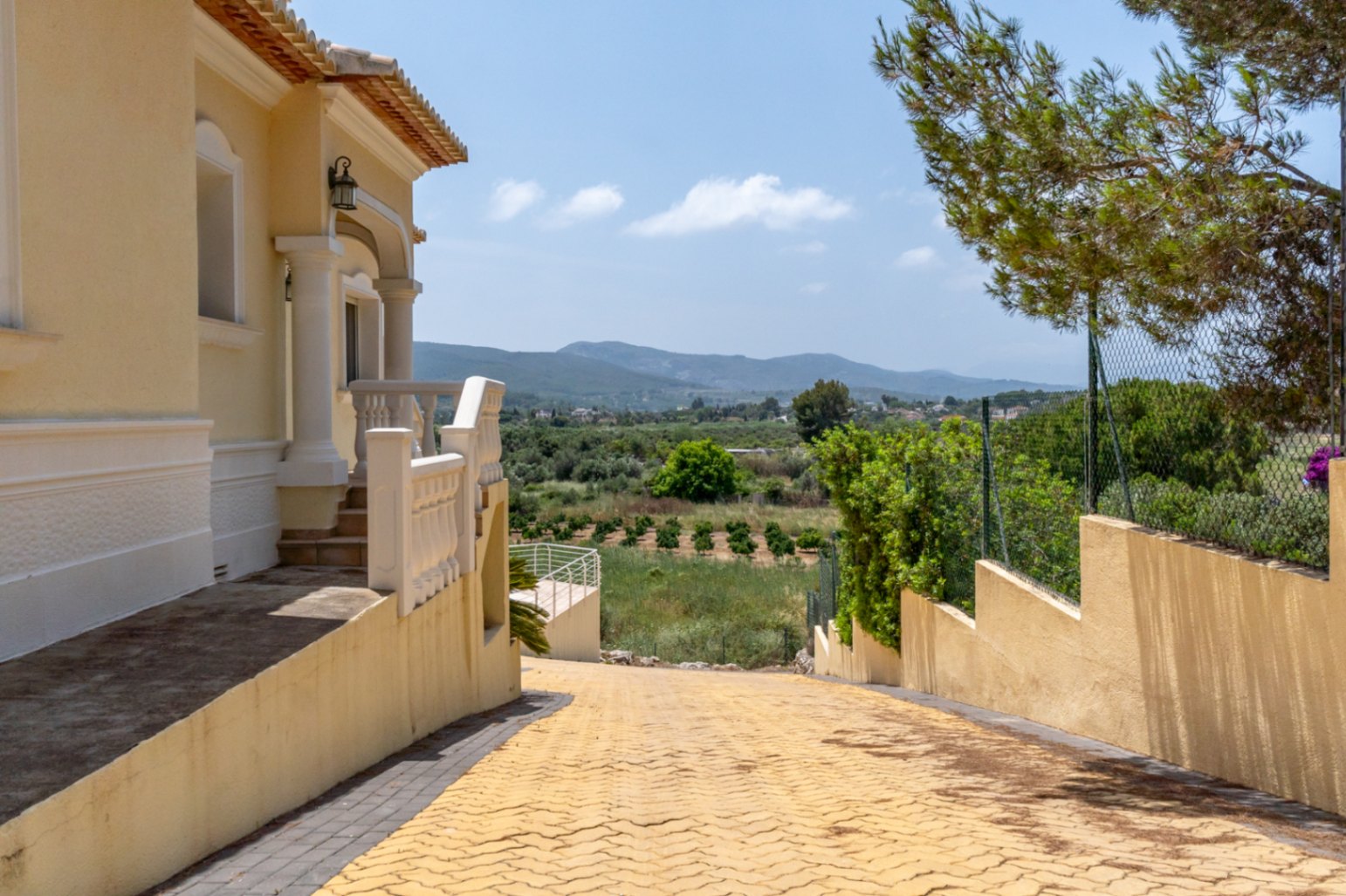 Entrée de la villa avec une allée pavée et un porche à colonnes, offrant une vue panoramique sur la vallée et les montagnes environnantes.