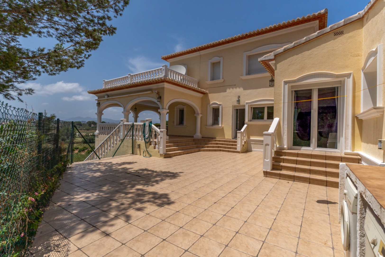 Grande terrasse carrelée avec naya à arcades, balustrades blanches, coin buanderie extérieur et vue dégagée sur la vallée environnante.