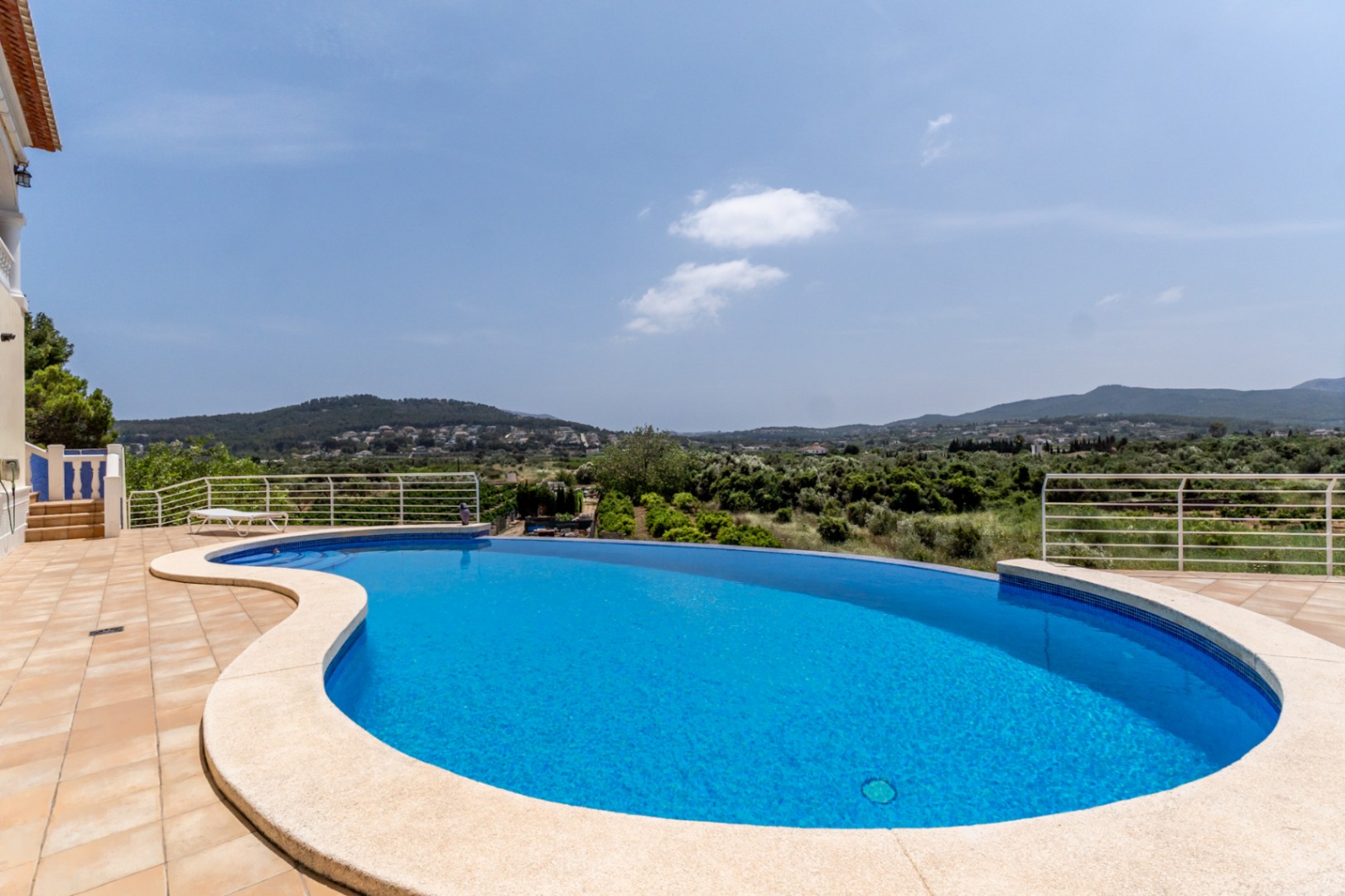 Piscine à débordement aux formes courbes avec terrasse en terre cuite, offrant une vue panoramique imprenable sur la vallée et les collines environnantes.