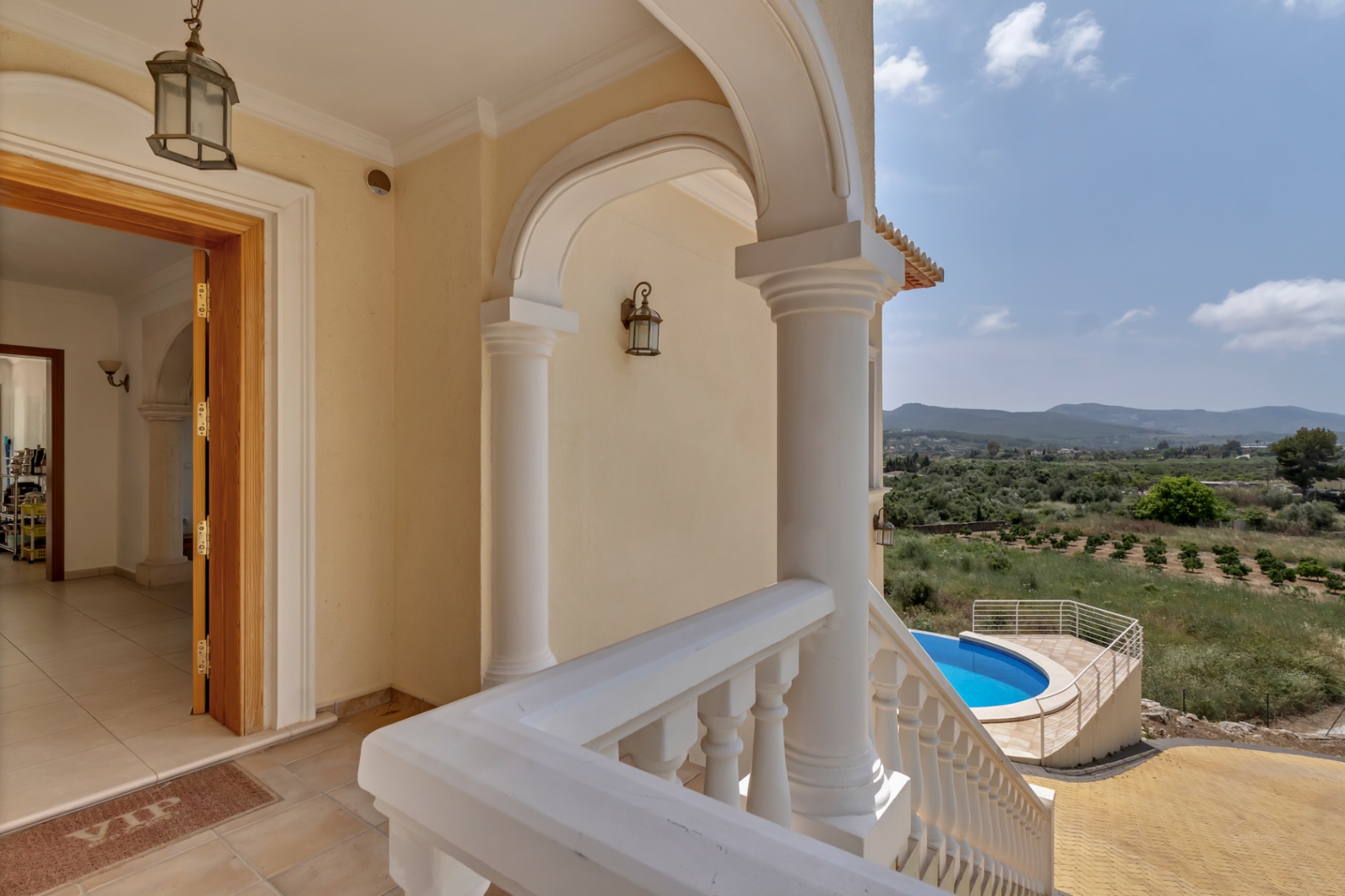 Porche d'entrée avec colonnes et balustrades blanches, offrant une vue sur la piscine circulaire et le paysage montagneux environnant.