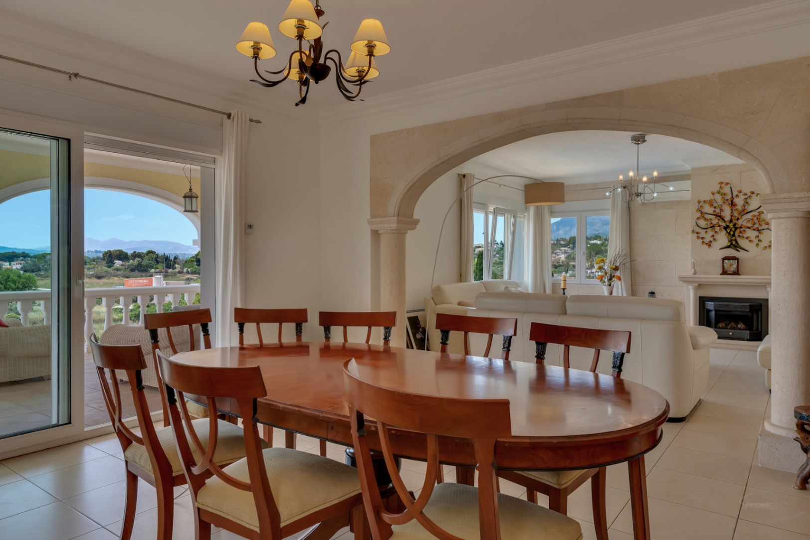 Salle à manger lumineuse avec table en bois, séparée du salon par une arche en pierre de Tosca, offrant un accès à la terrasse et des vues sur la vallée.