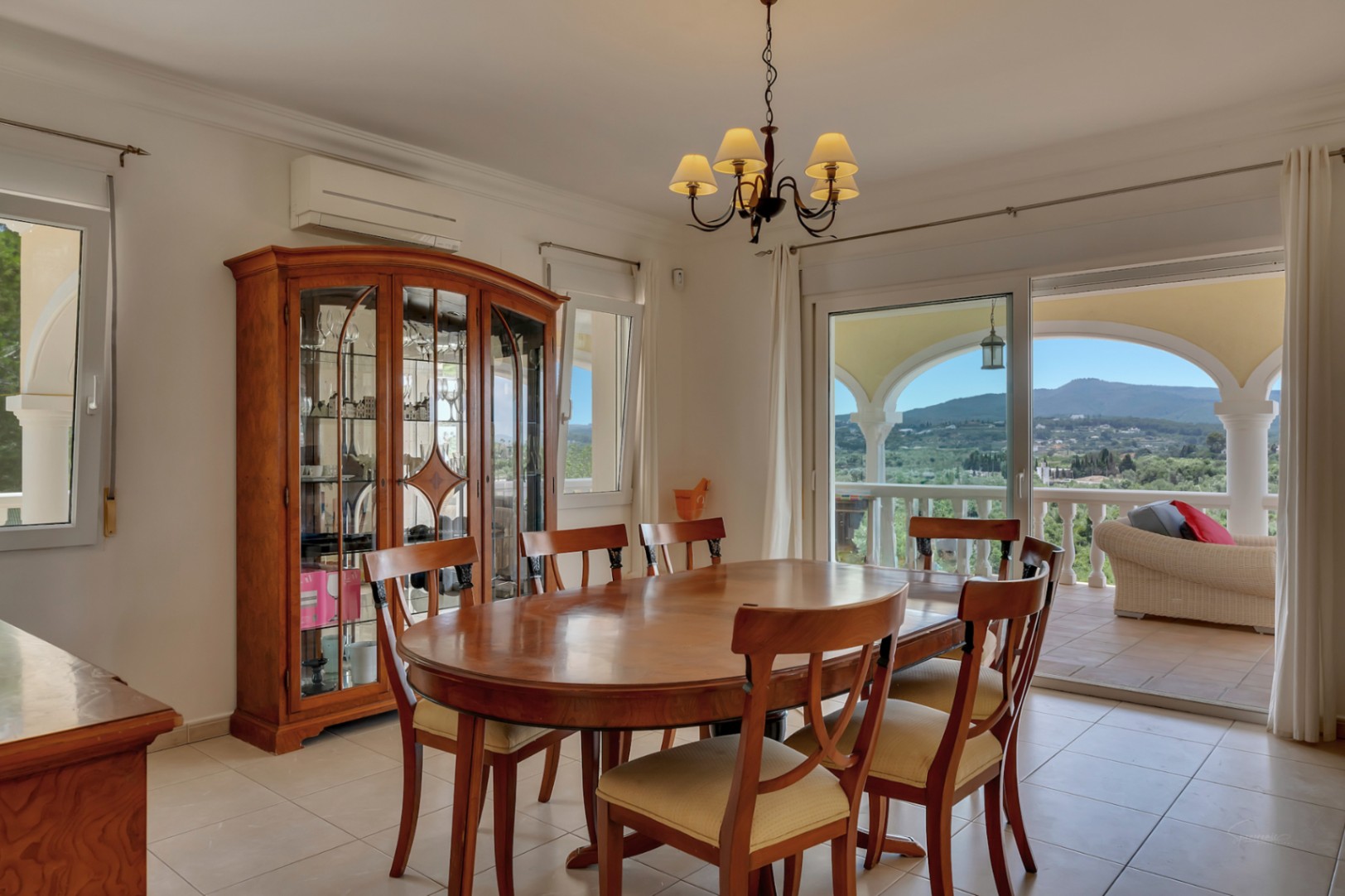 Salle à manger spacieuse avec table ovale en bois, vitrine classique et accès direct à la terrasse couverte offrant une vue panoramique sur la vallée.