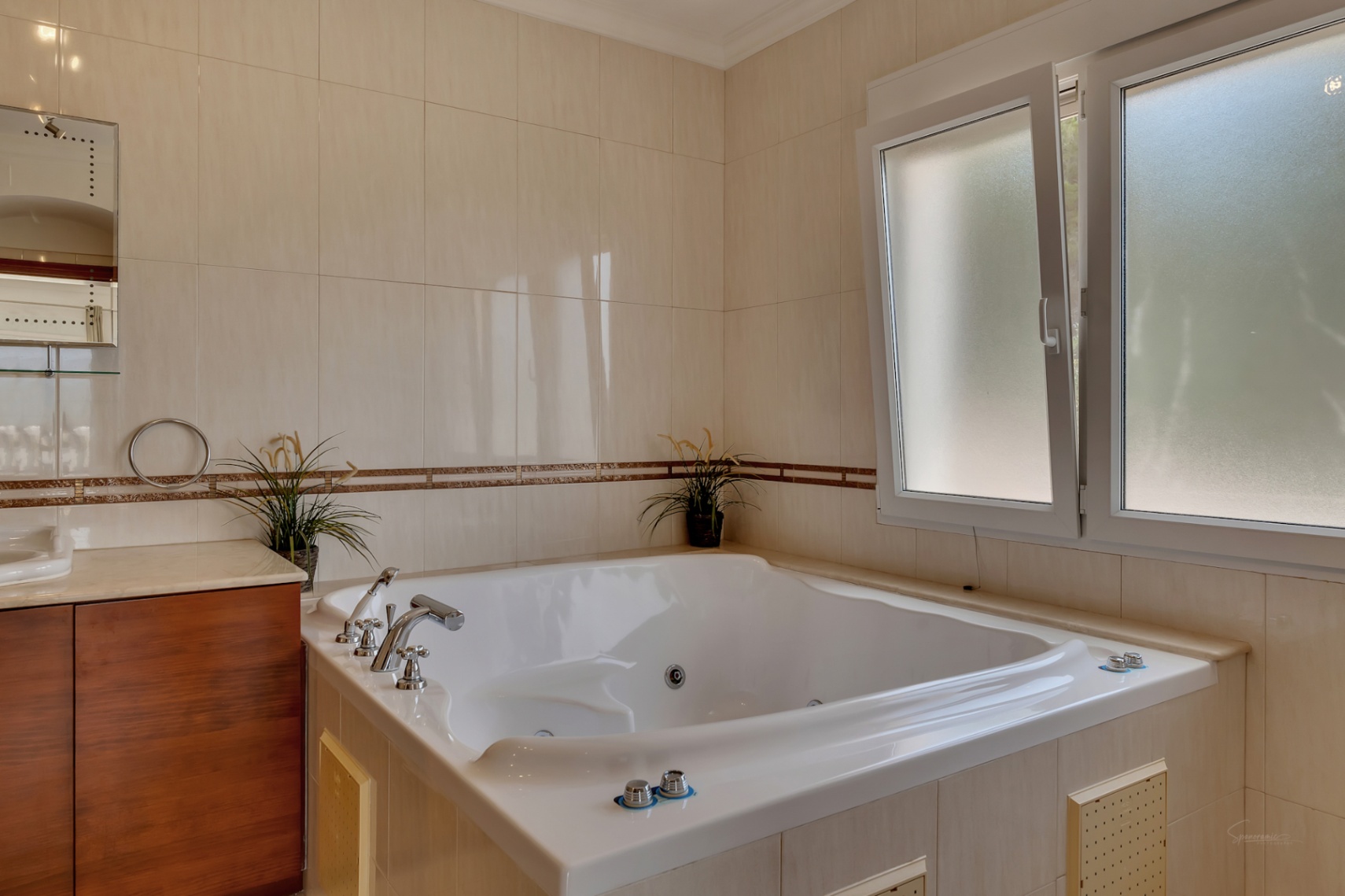 Salle de bain avec baignoire d'hydromassage encastrée, murs carrelés en tons crème avec frise décorative et fenêtre en verre dépoli offrant une lumière naturelle.