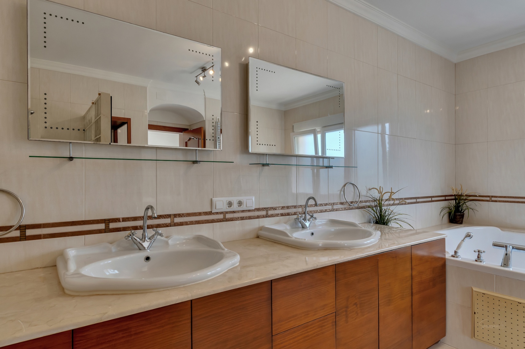 Salle de bain avec double vasque sur plan en marbre, meubles en bois, miroirs rétroéclairés et baignoire intégrée.