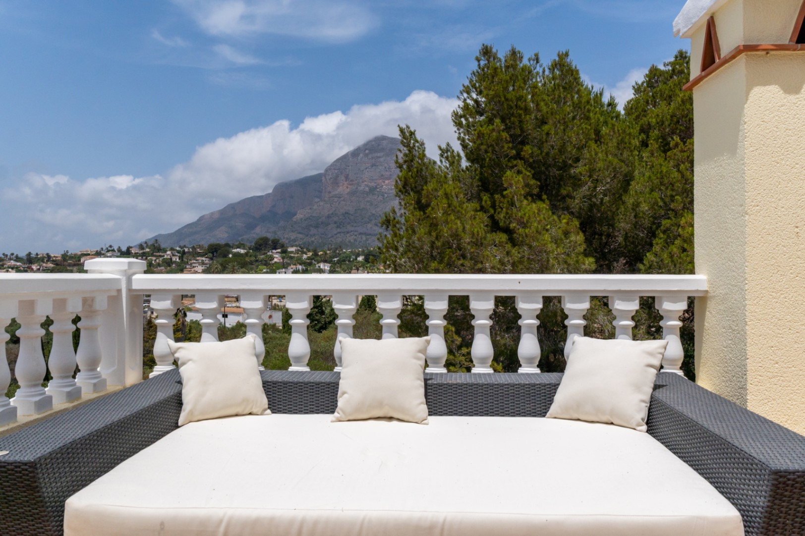 Terrasse supérieure avec lit de jour en rotin et balustrade blanche, offrant une vue panoramique sur le mont Montgó et la vallée environnante.