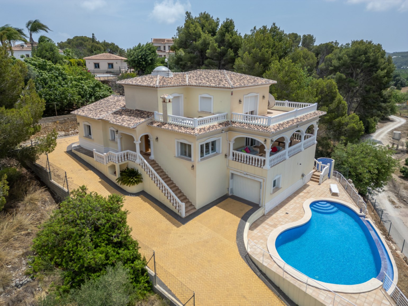 Vue aérienne de la villa méditerranéenne avec piscine de forme libre, vastes terrasses à balustrades blanches, naya voûtée et dôme vitré sur le toit.