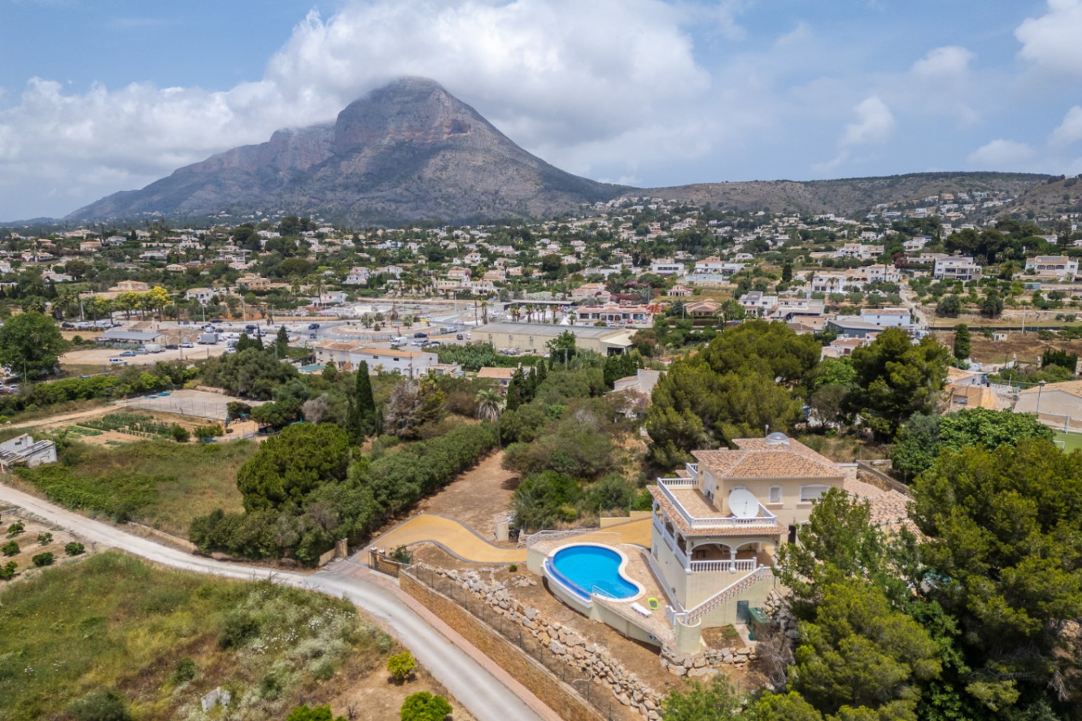 Vue aérienne de la villa mettant en valeur la piscine incurvée et les terrasses surplombant la vallée avec le mont Montgó en arrière-plan.