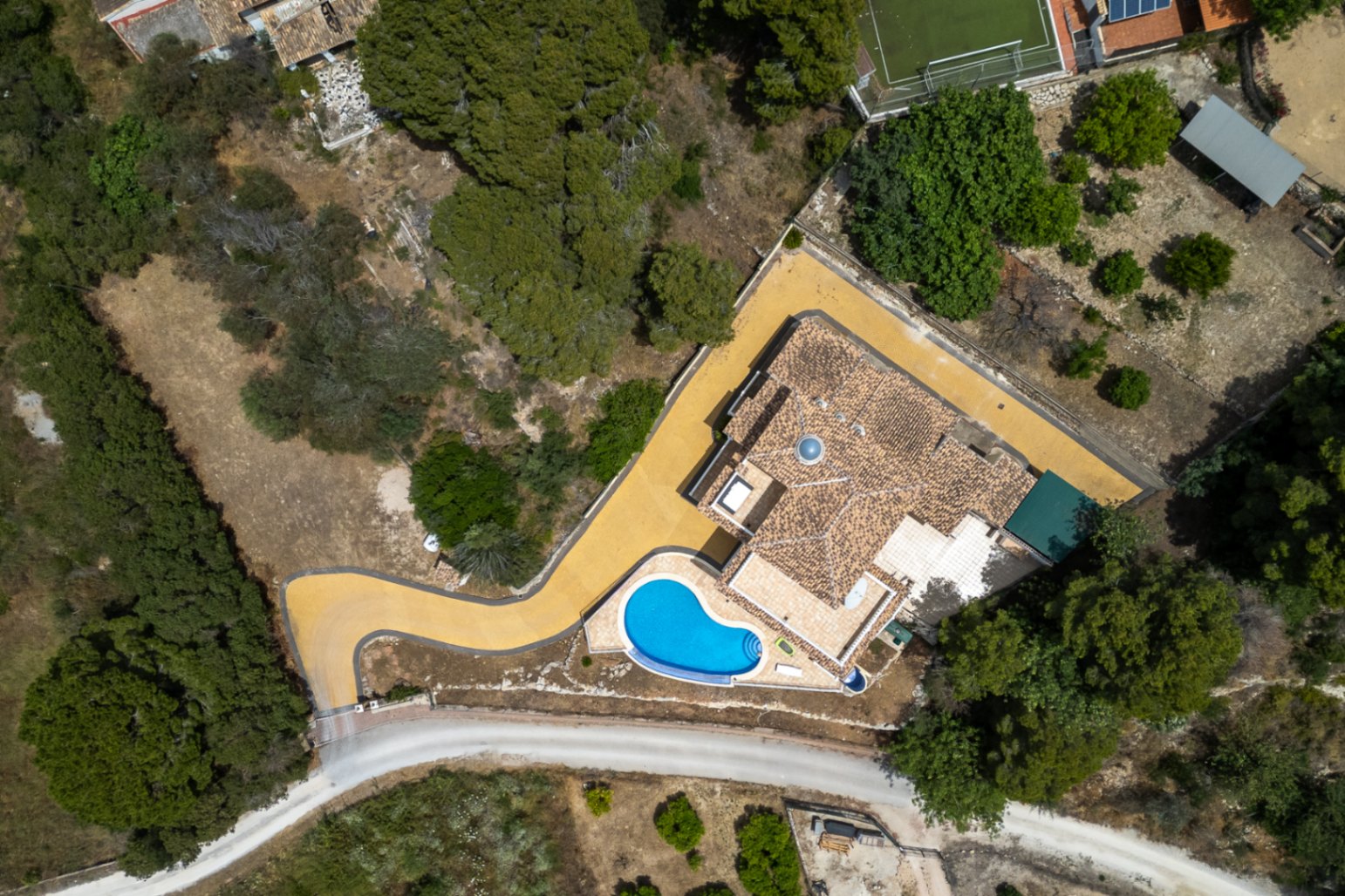 Vue aérienne de la villa montrant le toit en tuiles avec sa coupole centrale, la piscine à débordement et l'allée pavée serpentant à travers la végétation locale.